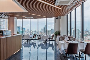Restaurante moderno com vista para a cidade, apresentando teto de madeira, janelas amplas e piso lustroso.