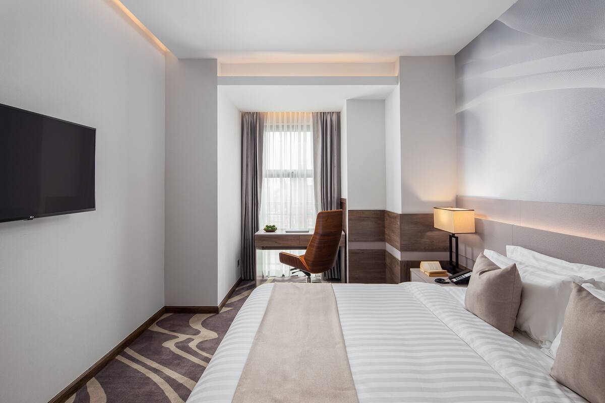 Una camera d'albergo con un letto, una scrivania, una sedia, un televisore e una lampada.