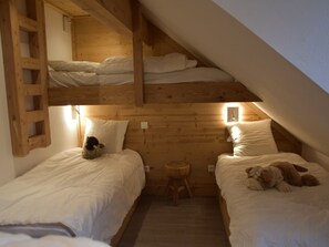 Een gezellig slaapkamer onder de dakpannen met twee stapelbedden, een klein houten krukje en een teddybeer op een van de bedden.