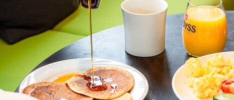 A breakfast setting with pancakes, toast, croissants, and orange juice on a table.