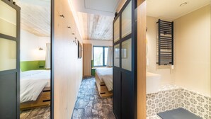 A narrow hallway leading to a room with a bed, a window, and a wooden ceiling. - De Brauhotel (Käerjeng)