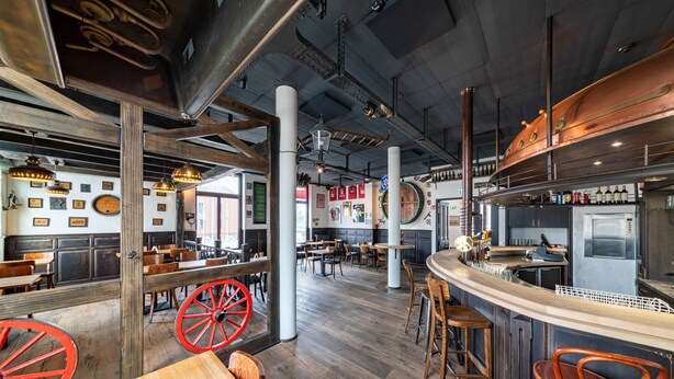 A spacious restaurant with high ceilings, exposed beams, and a mix of wooden and metal furnishings. - De Brauhotel (Käerjeng)