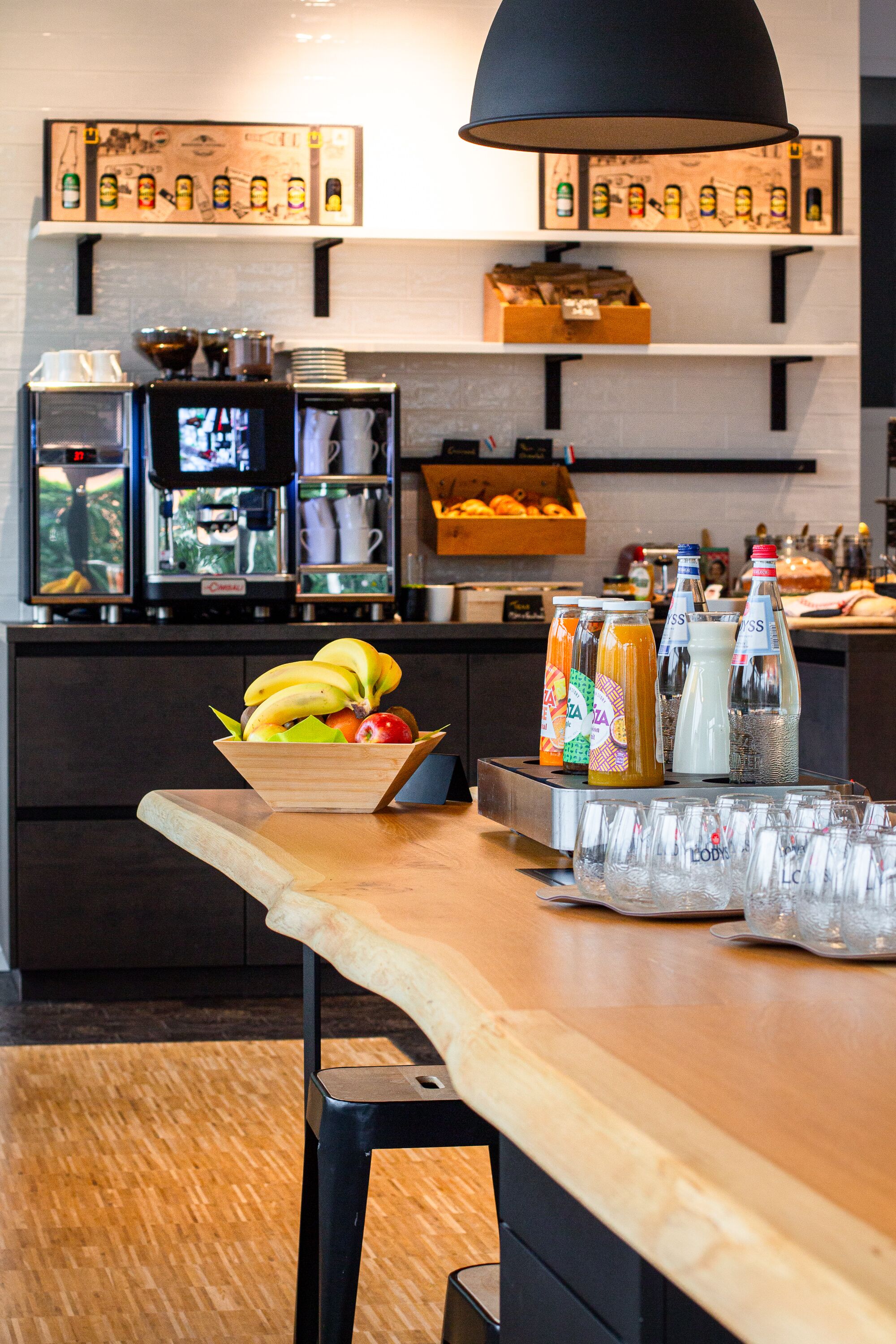 Una barra de desayuno con un bol de fruta, bebidas y una máquina de café.