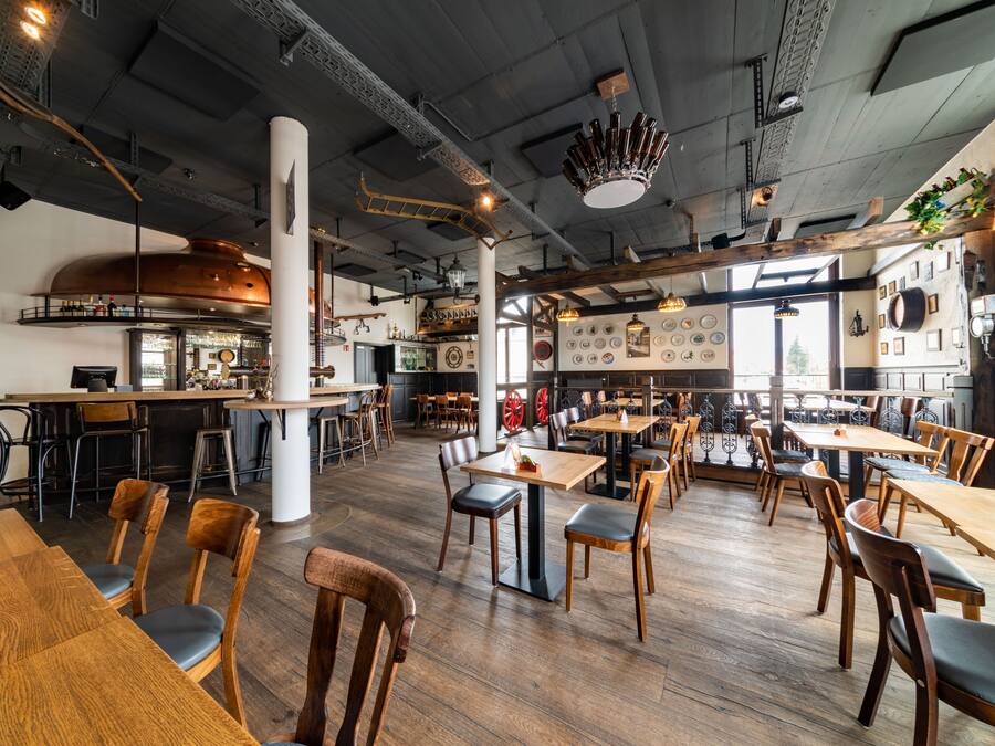Un restaurant spacieux avec des tables et des chaises en bois, un coin bar et une cuisine ouverte sur l’espace principal.