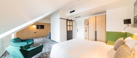 A modern hotel room with a large bed, a green sofa, a wooden wardrobe, and a television on the wall.