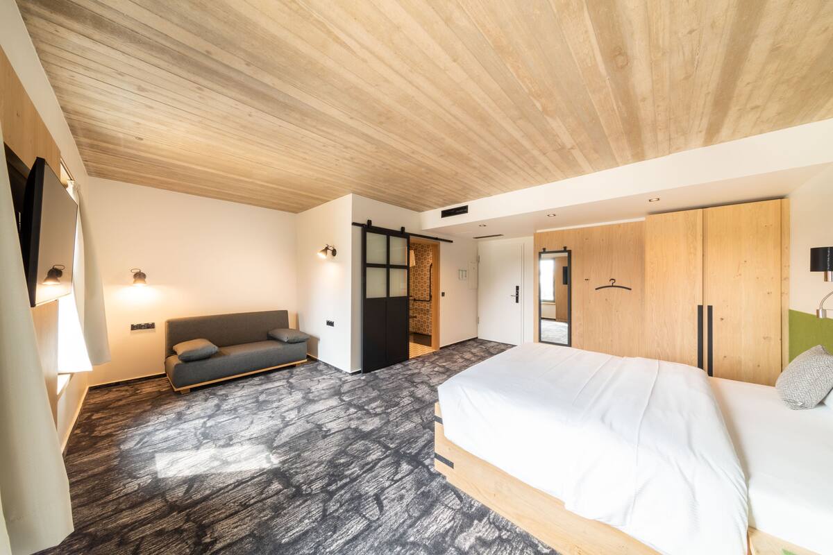 A modern bedroom with a large bed, a sofa, and a wooden wardrobe.