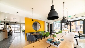 A modern interior with a wooden reception desk, yellow accent wall, and green seating area. - De Brauhotel (Käerjeng)