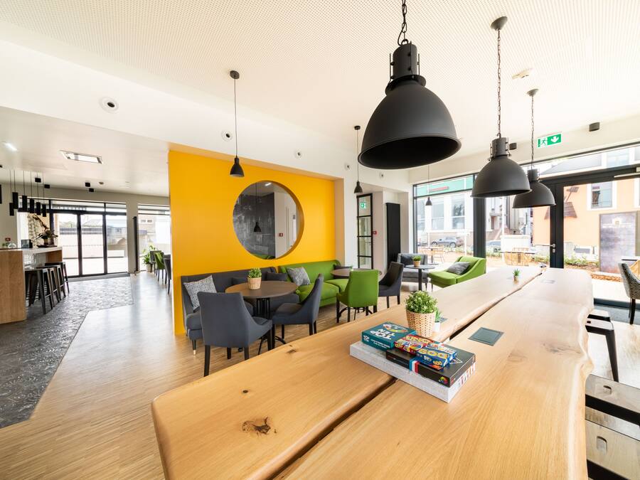 Un interior moderno con un mostrador de recepción de madera, una pared de acento amarilla y una zona de estar verde.