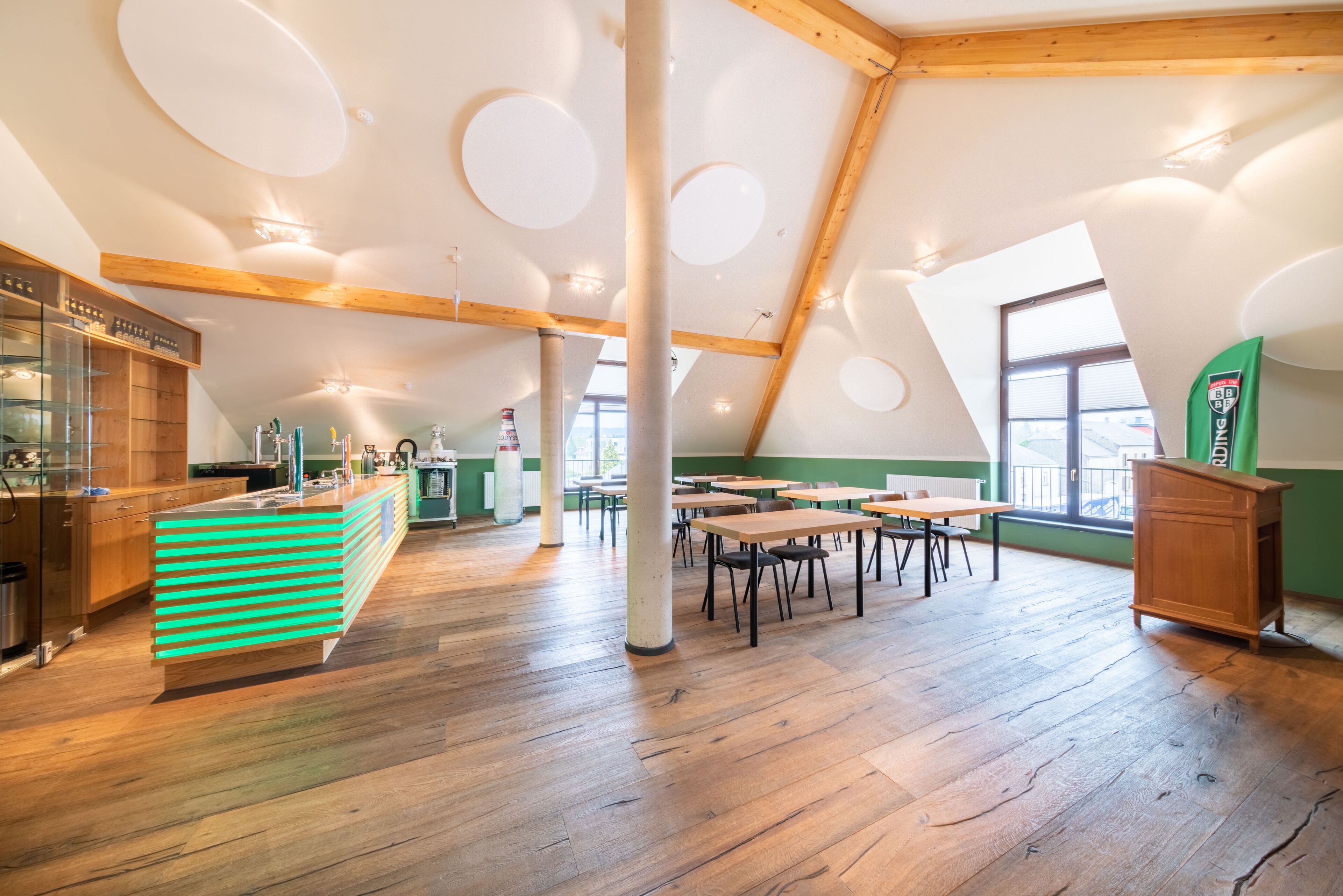 Amplia habitación con piso de madera, una barra verde y varias mesas y sillas.