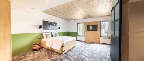 A bedroom with a wooden ceiling, a bed, a green wall, a window, and a TV.