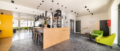 Un área de recepción moderna con un escritorio de madera, taburetes de bar y una silla verde.