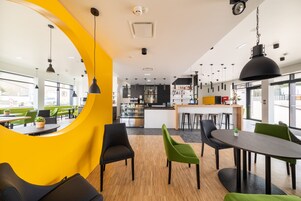 A modern dining area with a yellow accent wall, black and green chairs, and a central table.