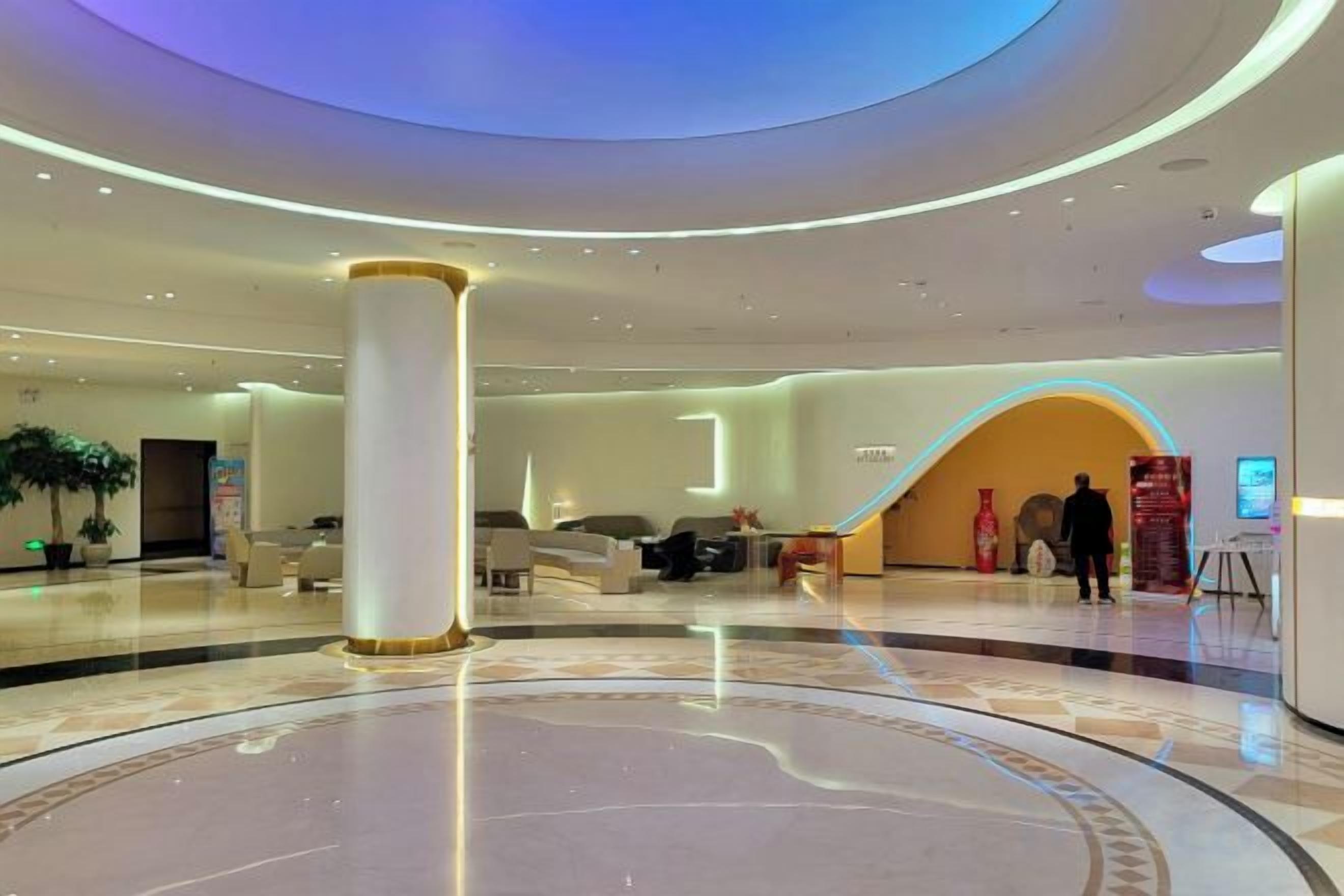 A modern hotel lobby with a central column, seating area, and a curved reception desk.