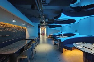 Un interior de restaurante moderno con una barra larga, zona de estar y un diseño de techo distintivo.