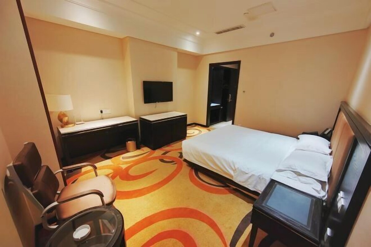 A hotel room with a bed, a desk with a chair, a TV, and a small table.