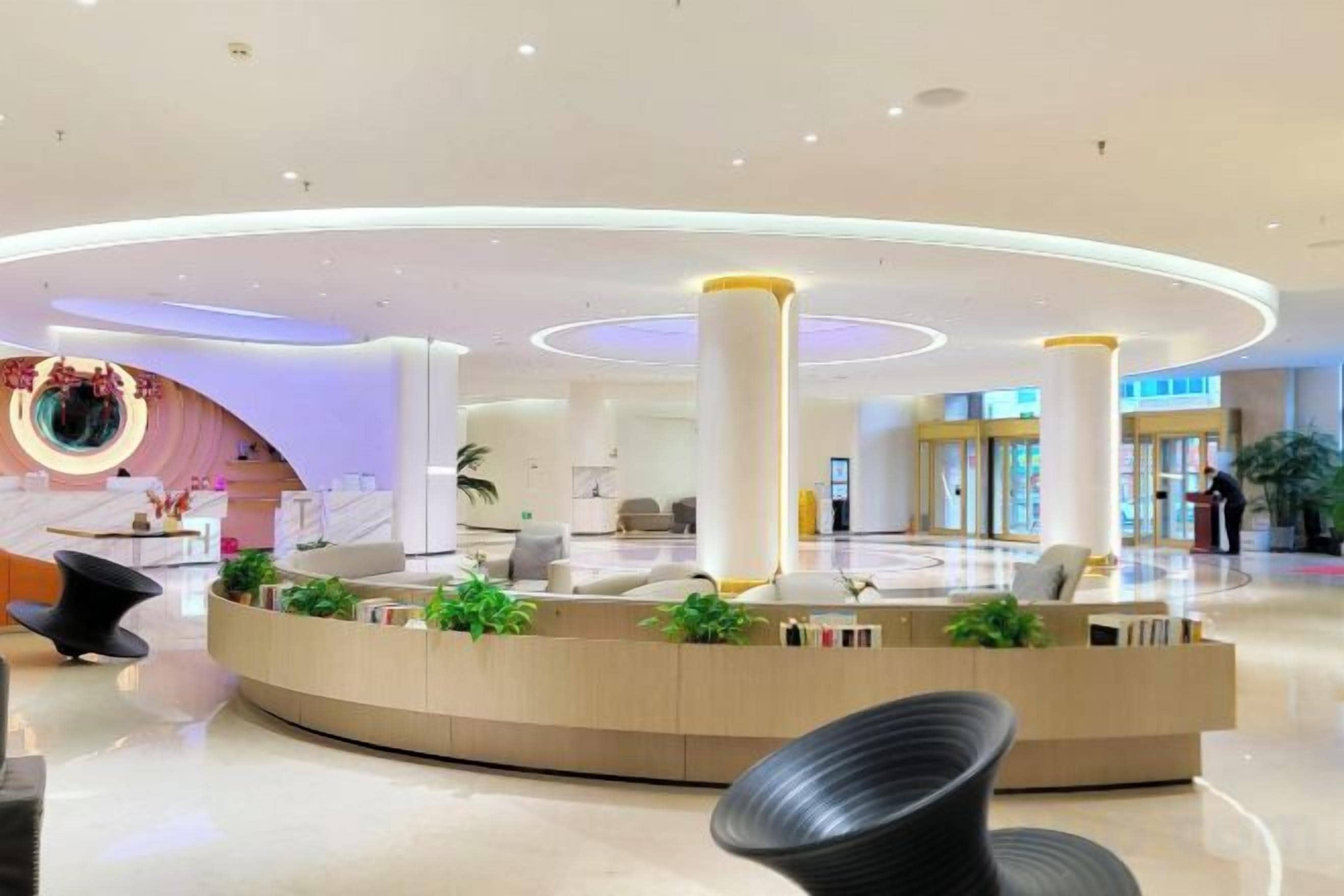 A modern lobby with a circular reception desk, seating area, and a large plant.