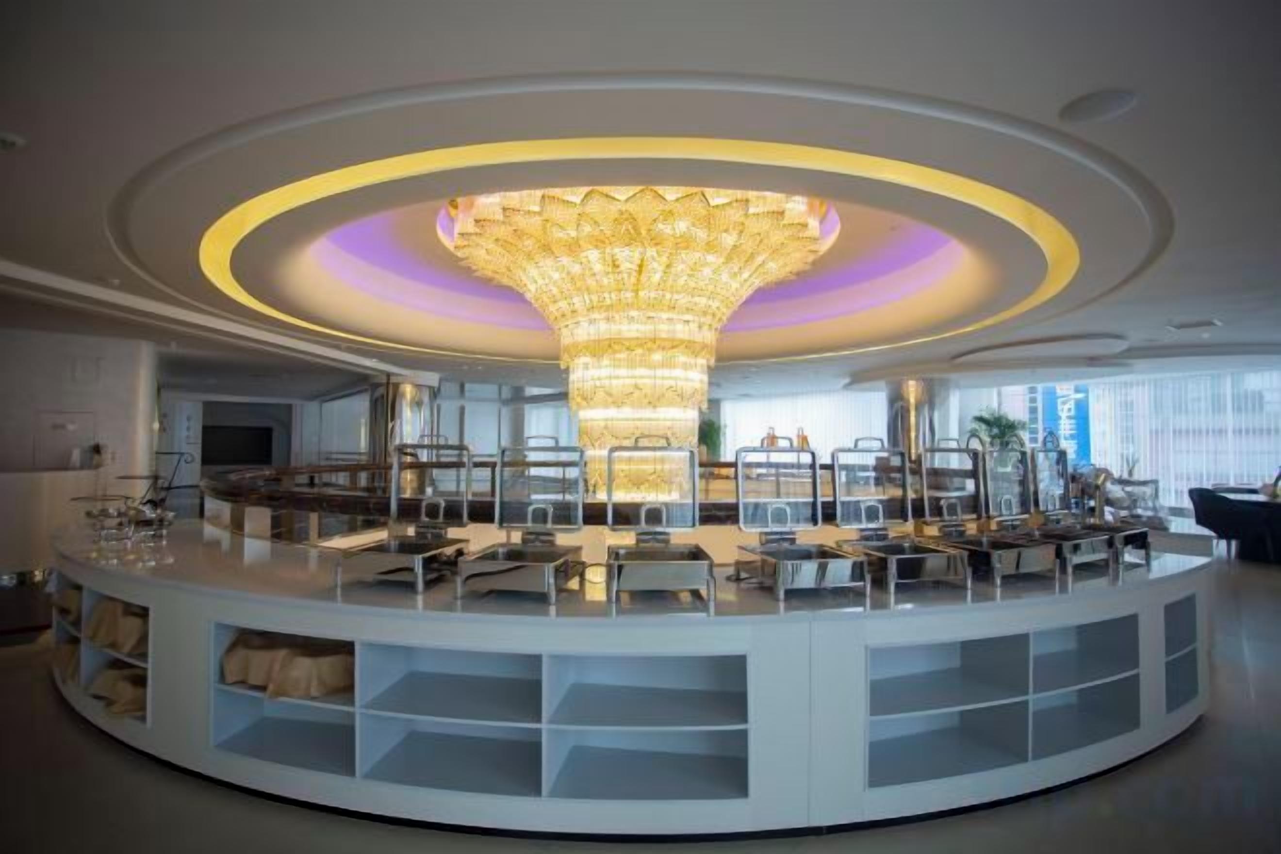 A modern, circular lounge area with a central chandelier, seating arrangements, and a white, curved structure.