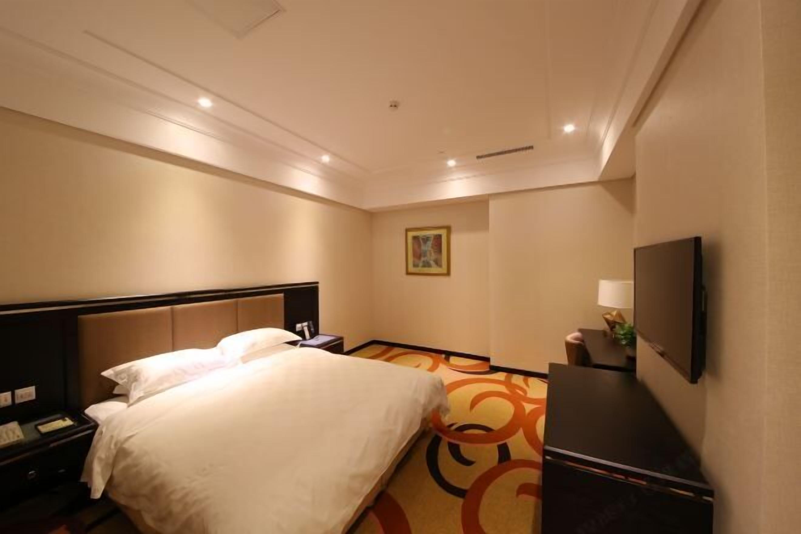 A hotel room with a large bed, a desk, a TV, and a painting on the wall.