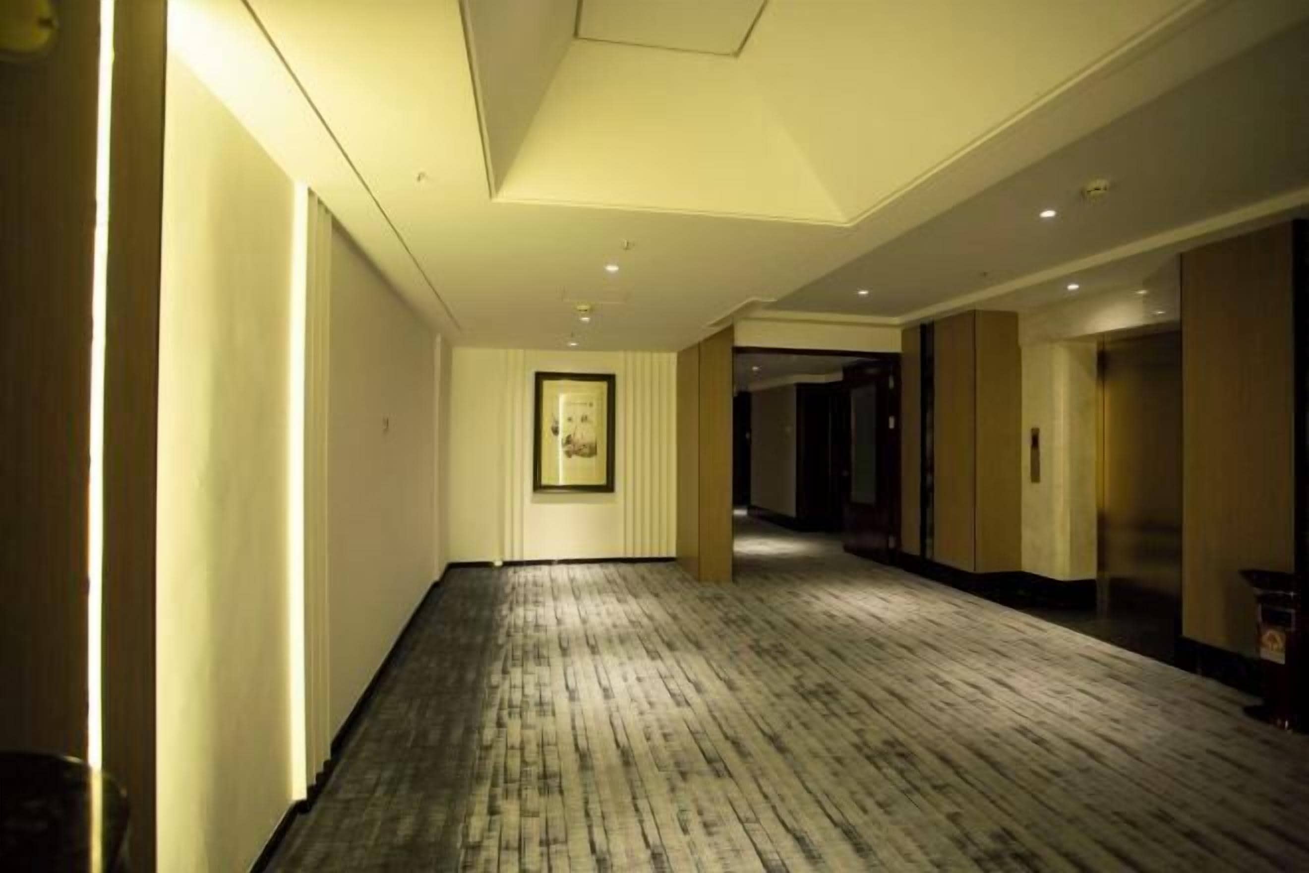 Un pasillo de hotel con piso de madera, obras de arte enmarcadas en la pared y puertas que dan a las habitaciones.
