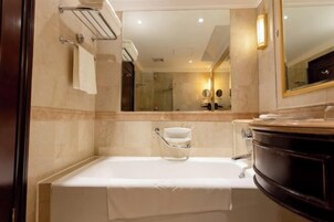 Un baño moderno con bañera, tocador con lavabo oscuro y un espejo grande.