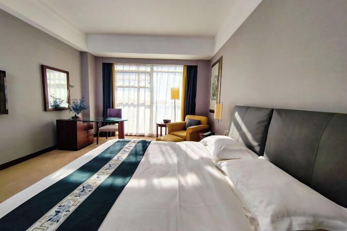 A hotel room with a large bed, a desk, a chair, and a window with curtains.