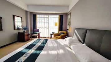Habitación de hotel con una cama grande, un escritorio, una silla y un ventanal con cortinas.