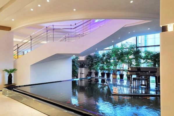A spacious indoor area with a reflective water feature, potted plants, and a piano.