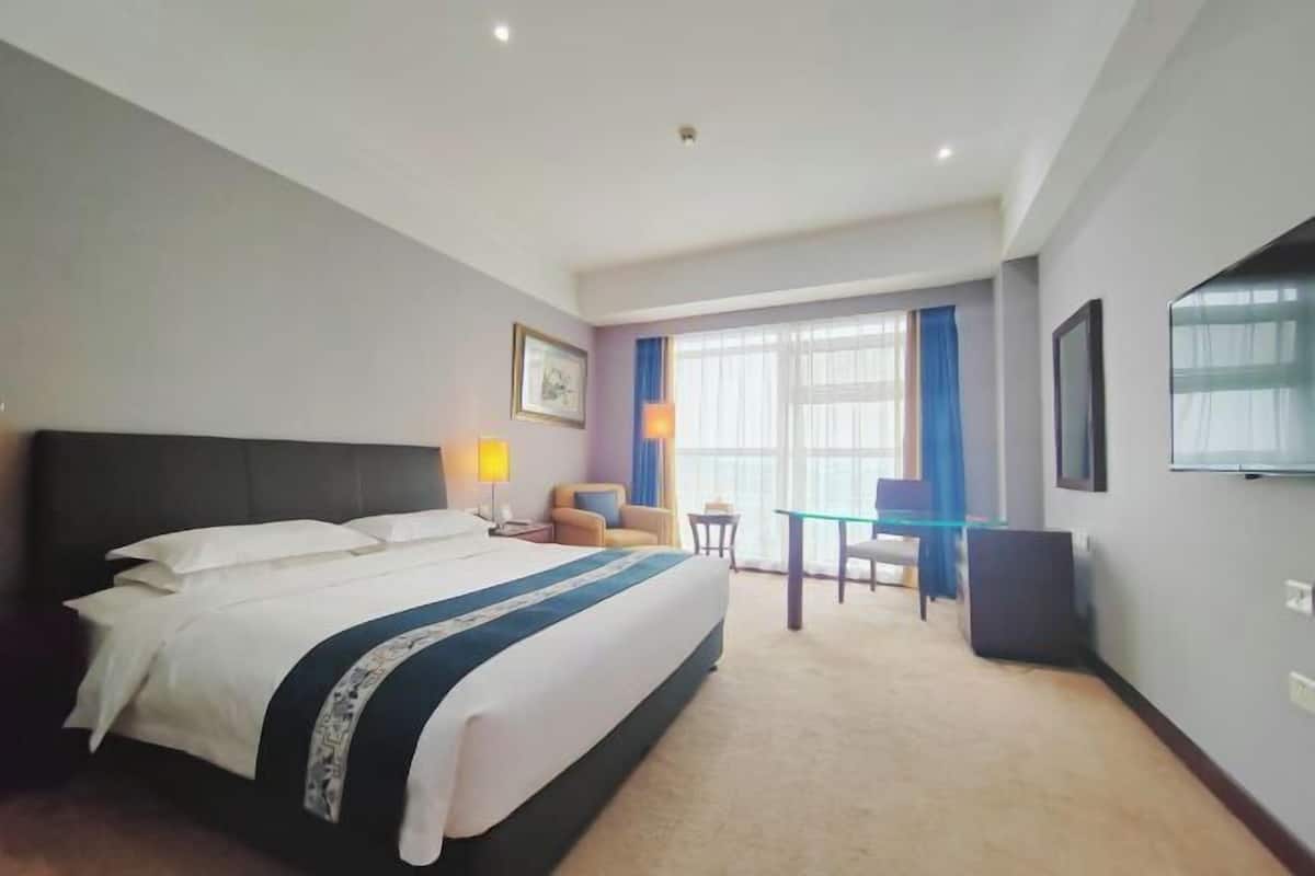 Une chambre d’hôtel avec un grand lit, un bureau, une chaise et un téléviseur.