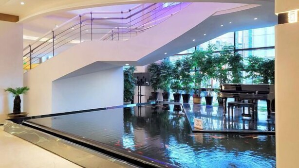 Een ruime atrium met een fontein, een piano en potplanten.