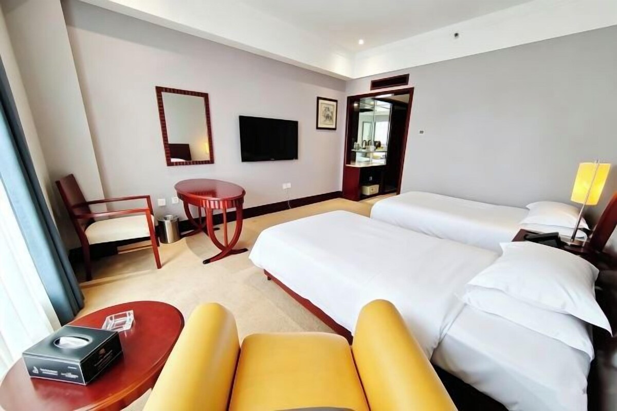 A hotel room with a large bed, a desk with a chair, a small table, and a television.