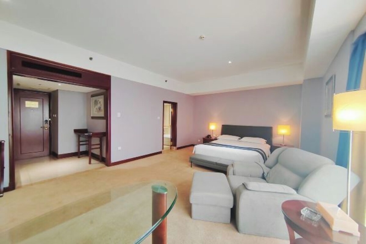 Une chambre d’hôtel avec un lit, un canapé, une table en verre et un bureau.