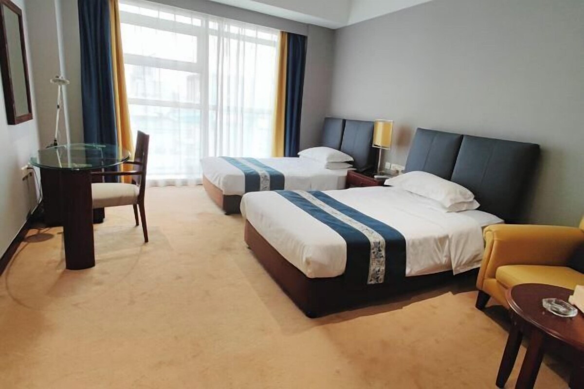 A hotel room with two beds, a desk, a chair, and a small table.