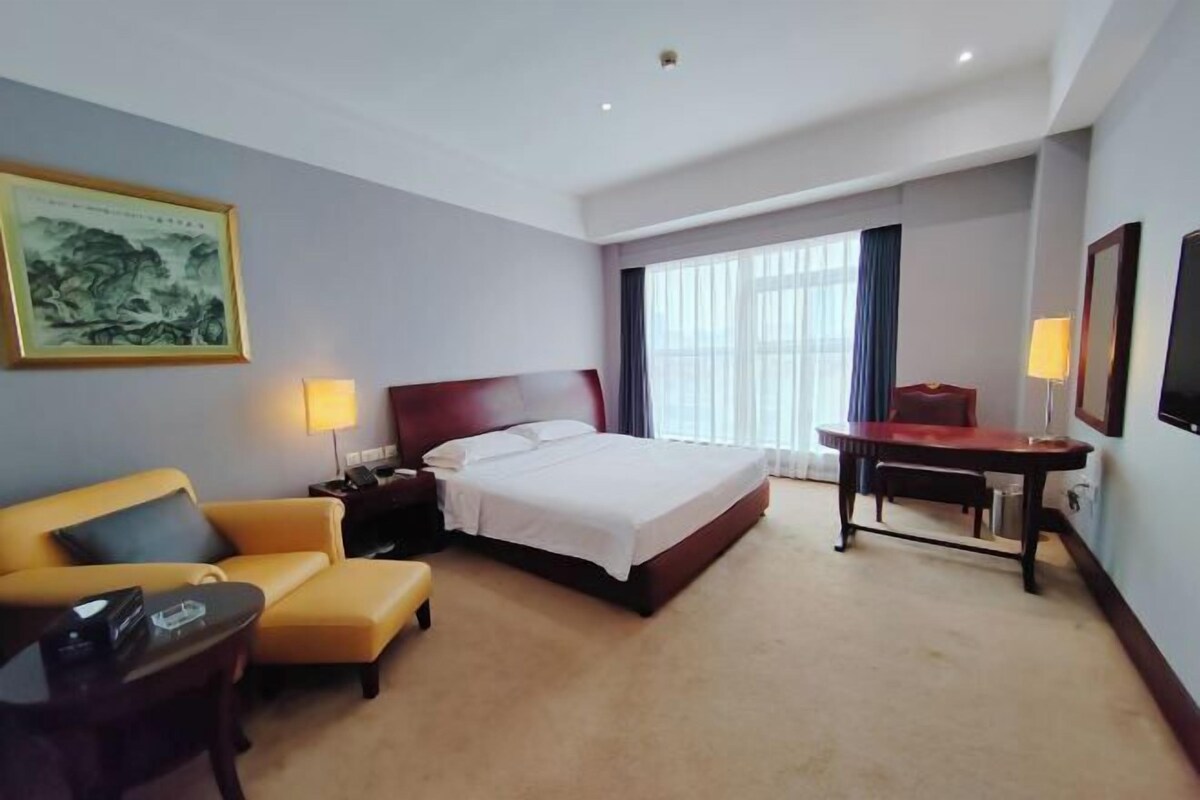 A hotel room with a bed, a desk, a chair, a sofa, and a painting on the wall.