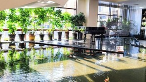 Ruime binnenruimte met een groot reflecterend waterkunstwerk, potplanten en een vleugelpiano.