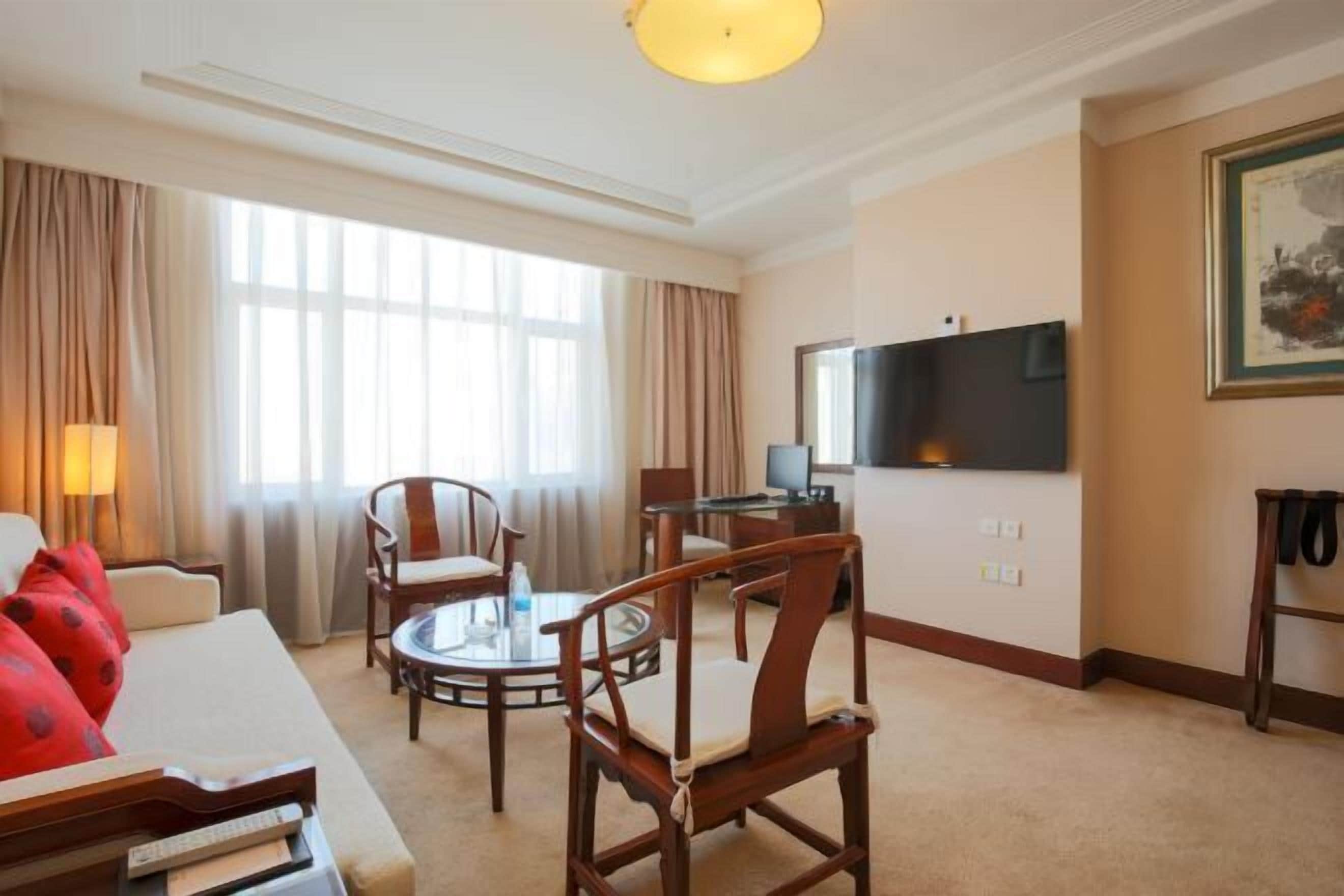 Habitación de hotel con sofá, dos sillones, una mesita redonda, televisor y un cuadro en la pared.