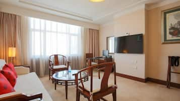 Habitación de hotel con sofá, dos sillones, una mesita redonda, televisor y un cuadro en la pared.