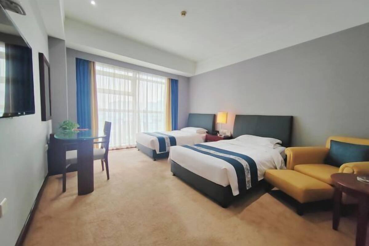 Une chambre d’hôtel avec deux lits, un bureau, une chaise, un canapé et un téléviseur.