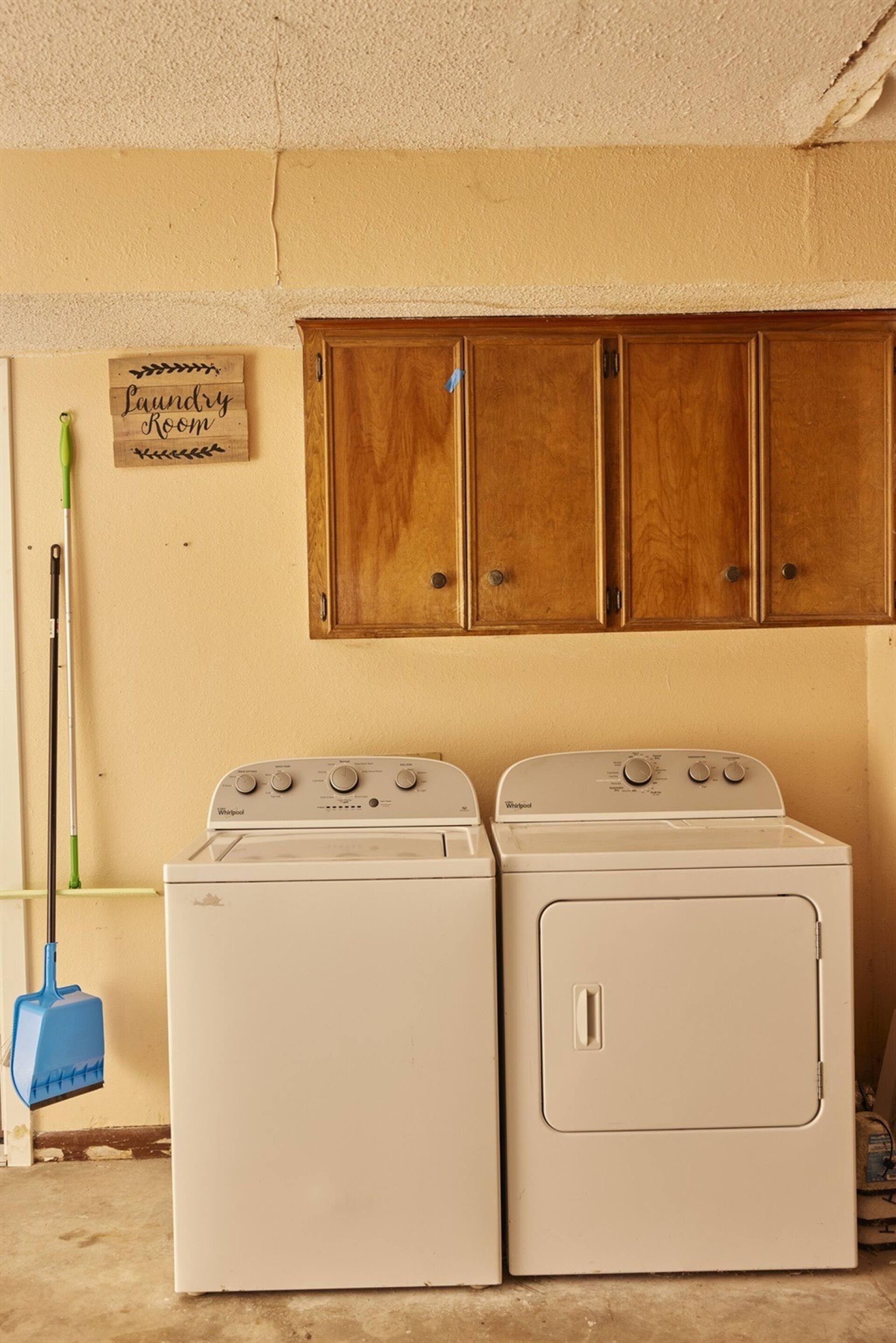 A laundry room with two stacked washers and dryers, wooden cabinets above, and a sign indicating the room's purpose.