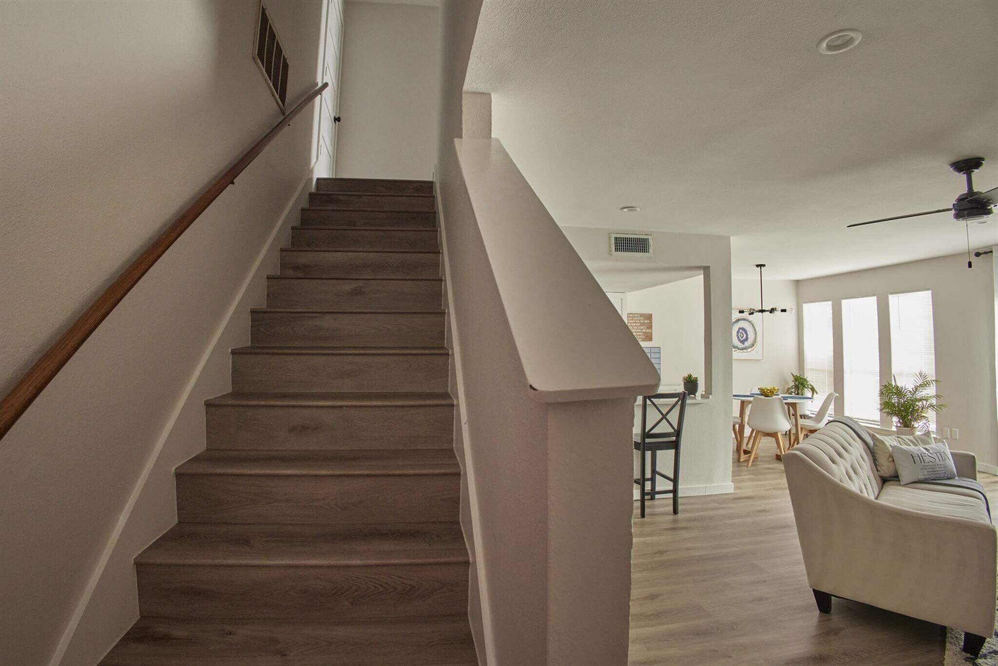 Escadaria que leva a uma sala de jantar com ventilador de teto e vista para a sala de estar.