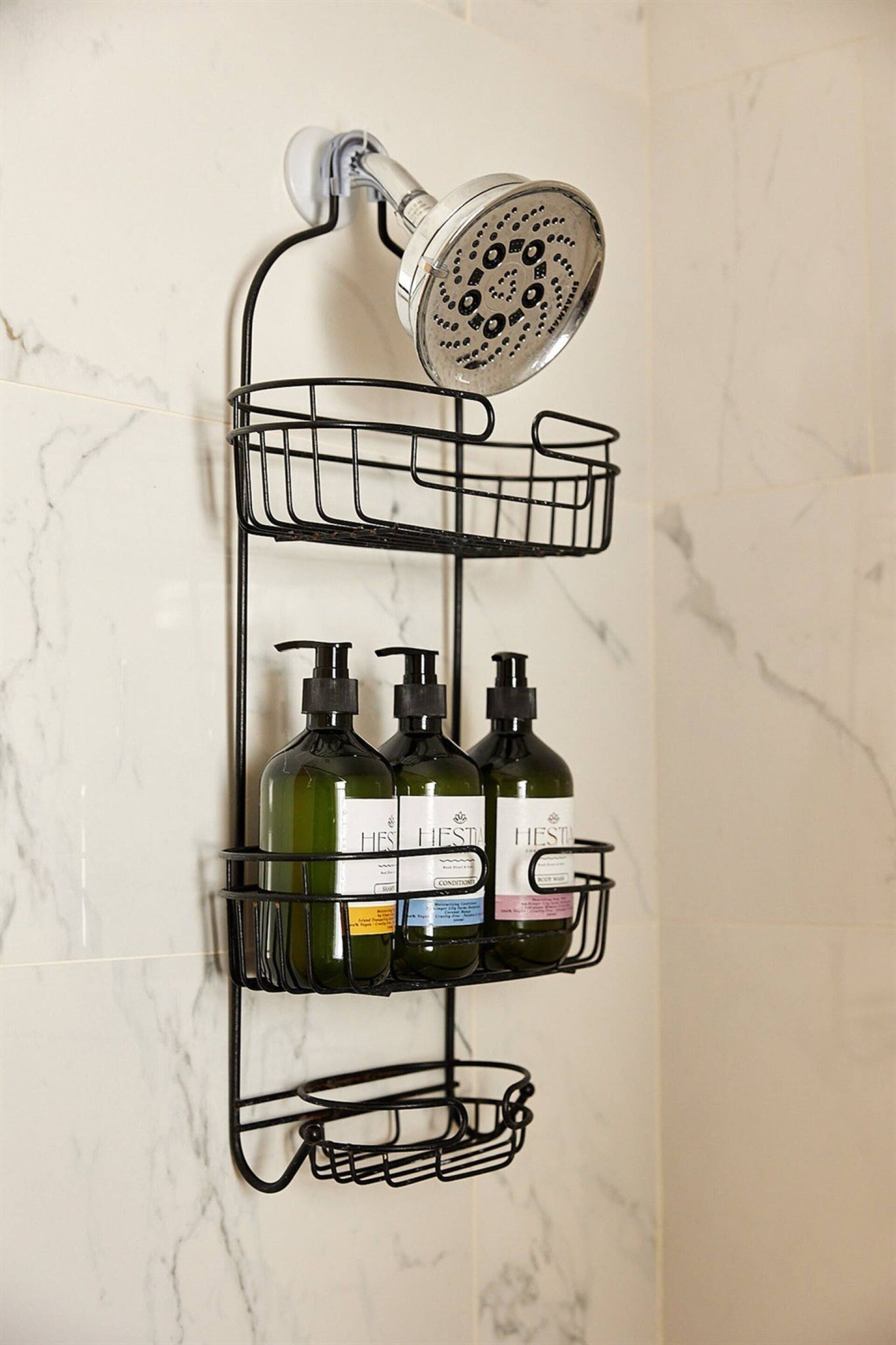 A bathroom with a shower, a marble wall, and a black metal shelf holding bottles.