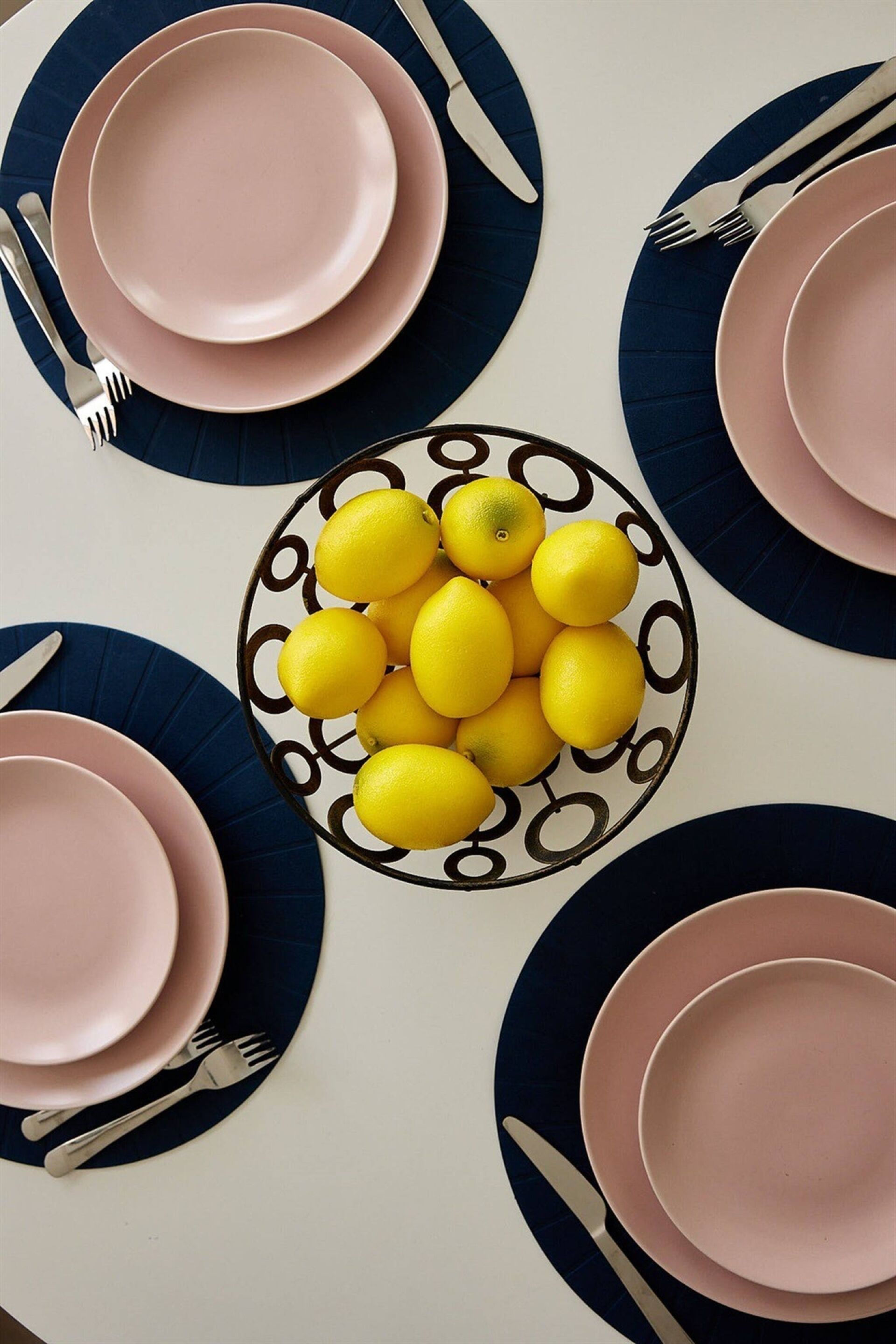 A table set with pink and blue plates, silverware, and a bowl of lemons.