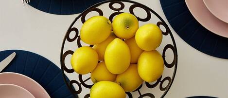 A table set with pink and blue plates, silverware, and a bowl of lemons.