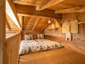 A cozy cabin room with a wooden ceiling, a bed with forest-themed bedding, and a small shelf with a lamp. - Cozy chalet for 6-8 with wood stove and sunny terrace (Notre-Dame-de-Bellecombe)