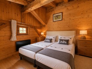 A wooden cabin bedroom with two beds, a window, a nightstand, and a framed picture on the wall. - Cozy chalet for 6-8 with wood stove and sunny terrace (Notre-Dame-de-Bellecombe)