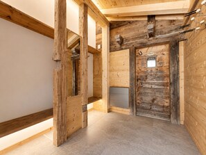 Interior de madera con vigas a la vista, una puerta con placa y piso de baldosas.