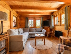 A cozy log cabin interior with a sectional sofa, a small table, and a television. - Cozy chalet for 6-8 with wood stove and sunny terrace (Notre-Dame-de-Bellecombe)