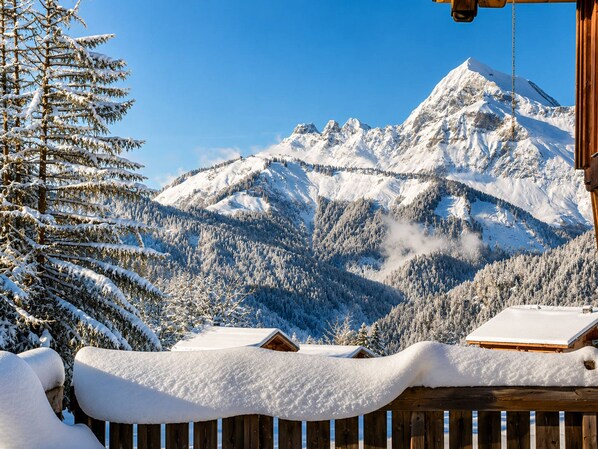 A wooden cabin with a snow-covered roof and a view of snow-covered mountains.
