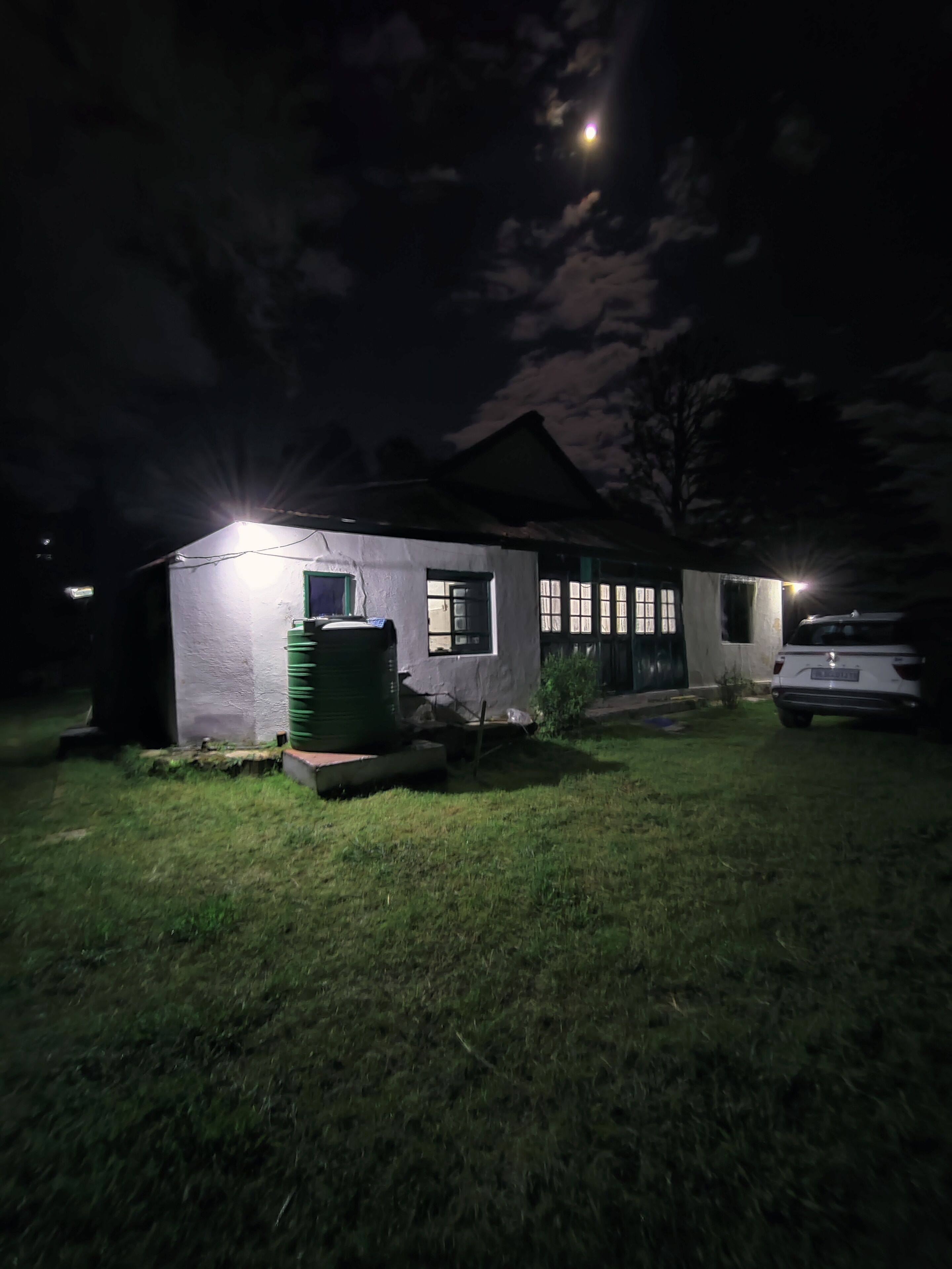 Una casa con exterior bien iluminado, un tanque de agua verde y un coche estacionado al frente.