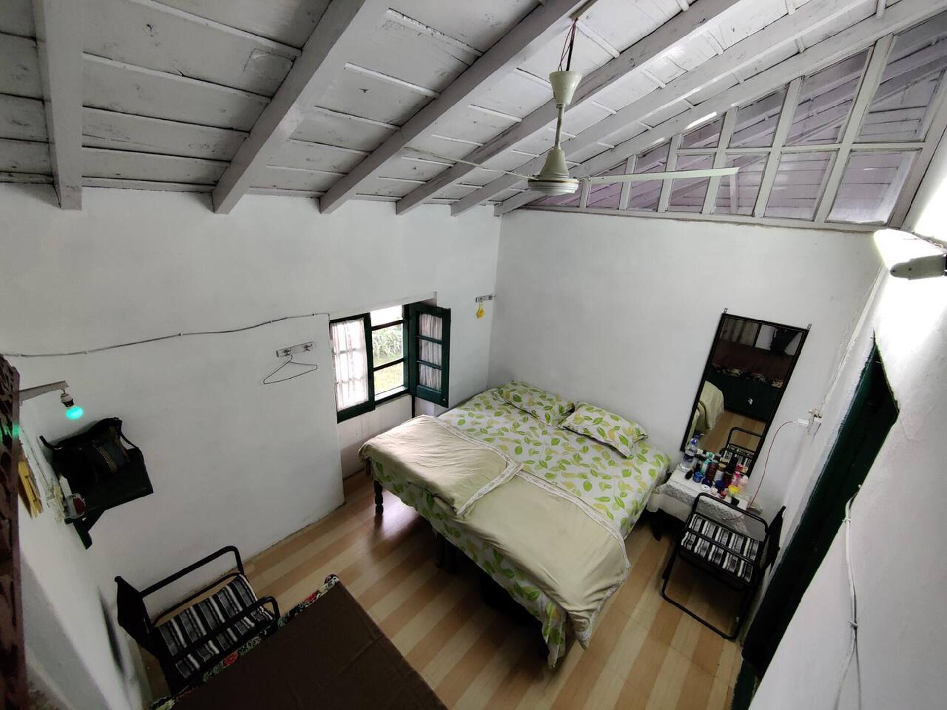 Un dormitorio con cama, escritorio, silla, ventana y ventilador de techo.