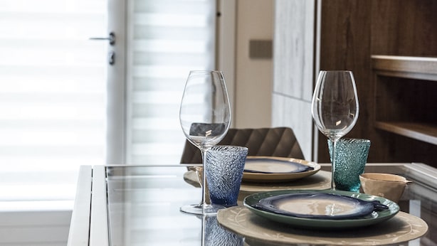 Une table à manger avec deux verres à vin et des assiettes, un vase en verre, et une porte en arrière-plan.